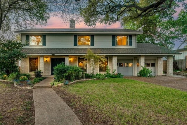 traditional-style house with a garage, a chimney, a front lawn, brick siding, and driveway