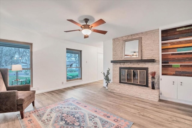 living area featuring a stone fireplace, light wood-style floors, and ceiling fan