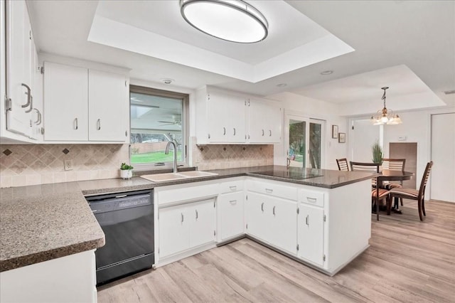 kitchen with a sink, a peninsula, black appliances, light wood-type flooring, and a raised ceiling