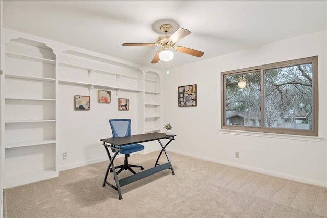office featuring a ceiling fan, light carpet, baseboards, and built in shelves