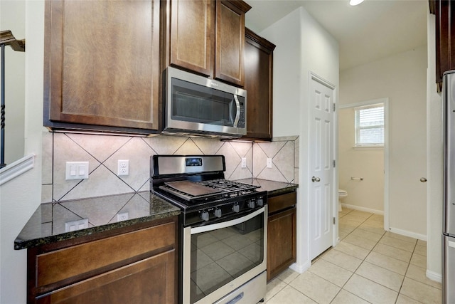 kitchen with decorative backsplash, dark brown cabinets, appliances with stainless steel finishes, dark stone counters, and light tile patterned flooring