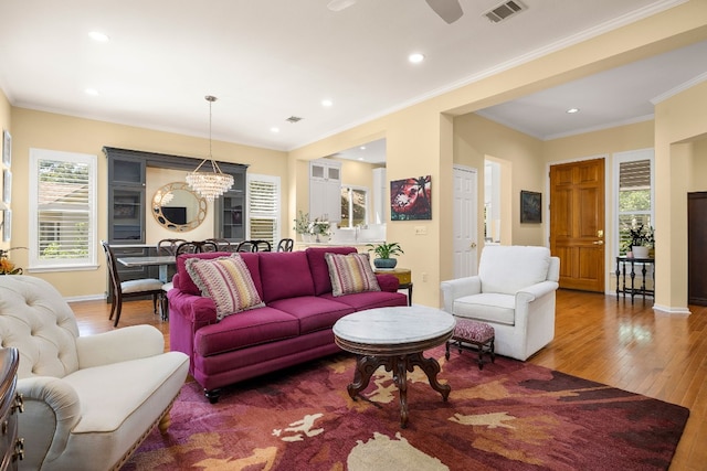 living room with crown molding, a healthy amount of sunlight, ceiling fan with notable chandelier, and hardwood / wood-style floors