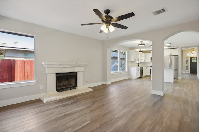 unfurnished living room with sink, light hardwood / wood-style flooring, a tiled fireplace, and ceiling fan