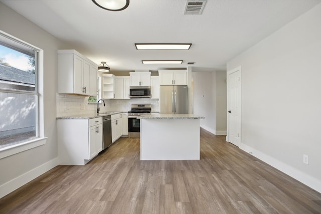 kitchen featuring sink, a kitchen island, white cabinetry, stainless steel appliances, and light hardwood / wood-style flooring