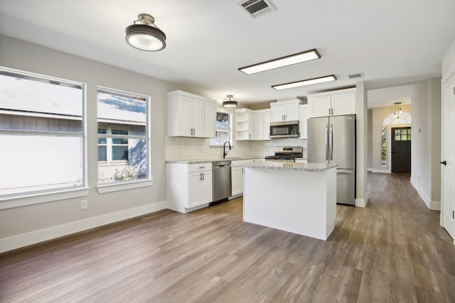 kitchen featuring a kitchen island, appliances with stainless steel finishes, white cabinetry, hardwood / wood-style flooring, and light stone counters