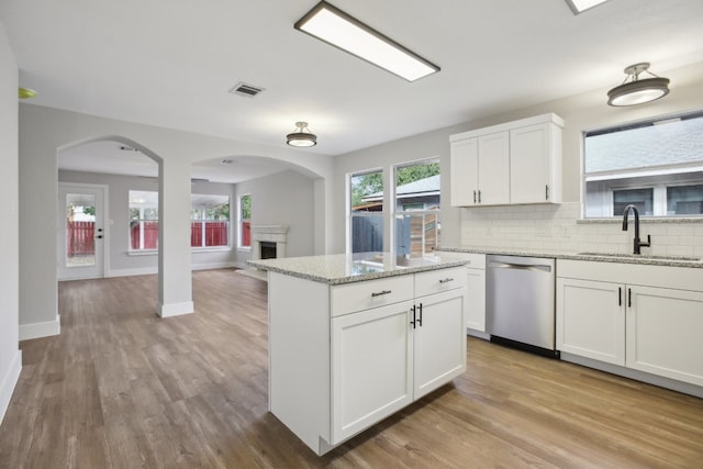 kitchen featuring sink, stainless steel dishwasher, white cabinets, light stone counters, and light hardwood / wood-style flooring