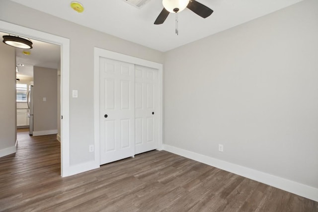 unfurnished bedroom with a closet, wood finished floors, freestanding refrigerator, and baseboards