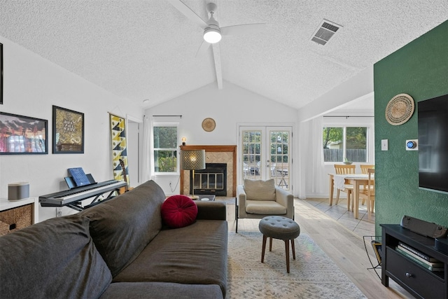 living room featuring lofted ceiling with beams, a textured ceiling, a tile fireplace, light hardwood / wood-style floors, and ceiling fan