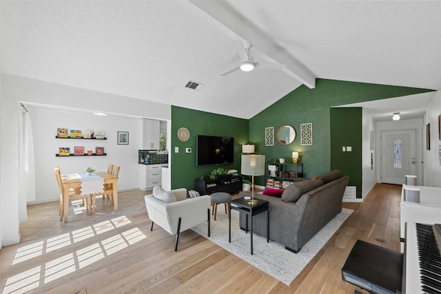 living room featuring lofted ceiling with beams, a textured ceiling, light hardwood / wood-style floors, and ceiling fan