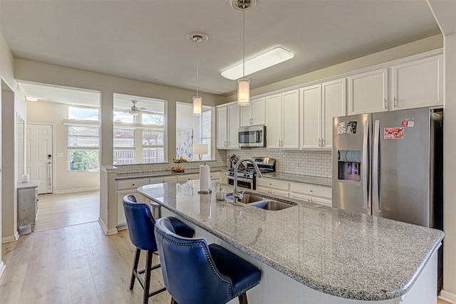 kitchen with white cabinets, a kitchen island with sink, light wood-type flooring, sink, and stainless steel appliances