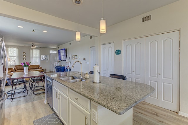 kitchen featuring hanging light fixtures, a center island with sink, light stone counters, light hardwood / wood-style flooring, and sink