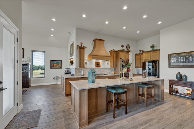 kitchen with a large island, a breakfast bar, light stone countertops, custom range hood, and light hardwood / wood-style floors