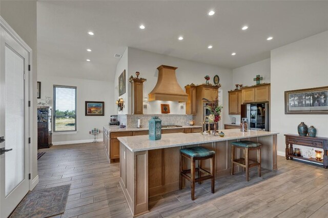 505 John Price St, Blanco, TX 78606 - kitchen featuring smart refrigerator, premium range hood, light wood finished floors, tasteful backsplash, and a large island with sink