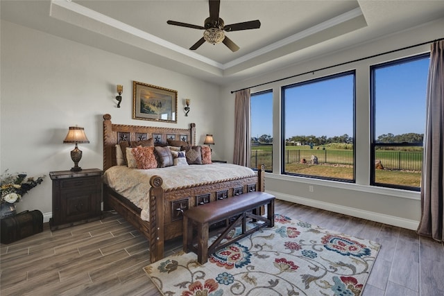 bedroom with ornamental molding, a raised ceiling, wood-type flooring, and ceiling fan