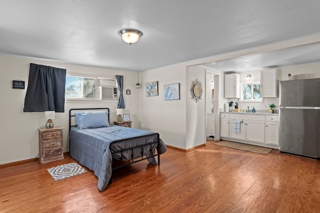 bedroom featuring ensuite bathroom, a textured ceiling, sink, light hardwood / wood-style flooring, and stainless steel refrigerator