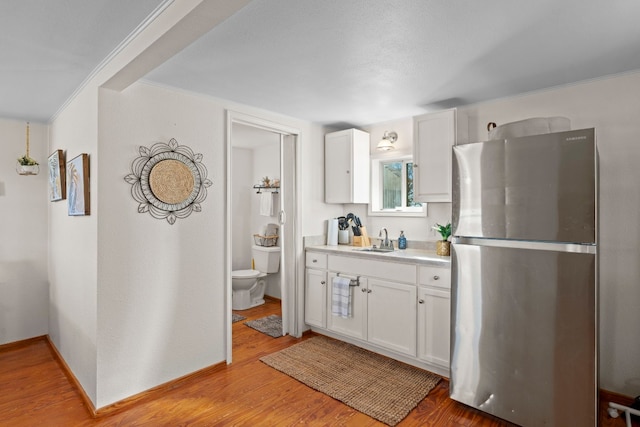 kitchen featuring stainless steel fridge, ornamental molding, sink, light hardwood / wood-style flooring, and white cabinetry