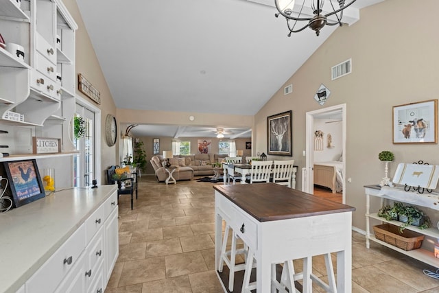 kitchen with white cabinets, ceiling fan with notable chandelier, high vaulted ceiling, and a breakfast bar area