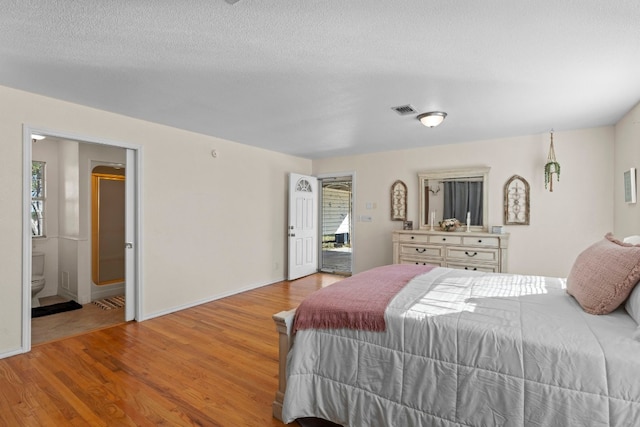 bedroom with a textured ceiling, connected bathroom, and light hardwood / wood-style flooring