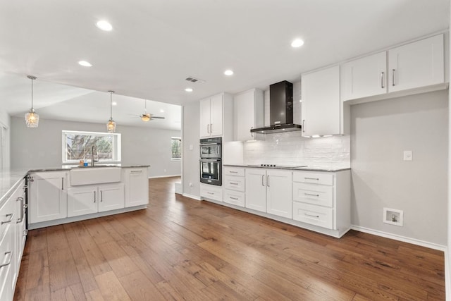 kitchen featuring tasteful backsplash, light wood-style floors, white cabinets, a sink, and wall chimney exhaust hood