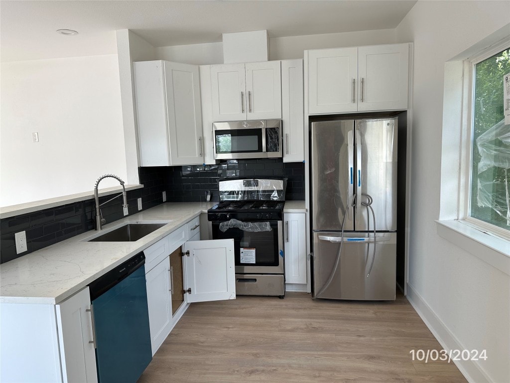 kitchen with decorative backsplash, white cabinets, appliances with stainless steel finishes, light wood-type flooring, and sink