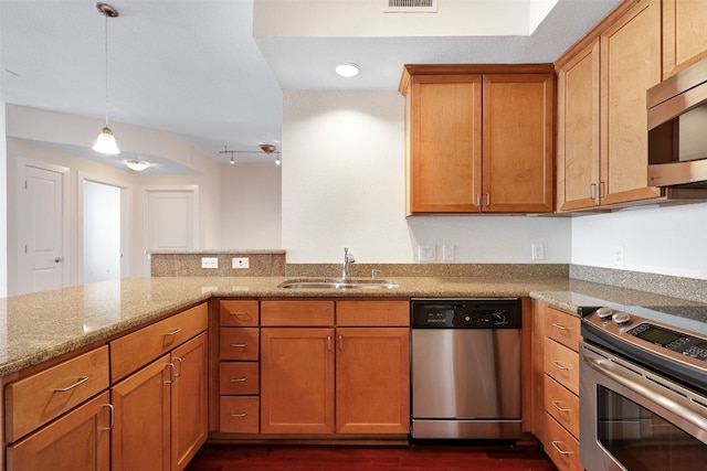 kitchen with kitchen peninsula, appliances with stainless steel finishes, light stone countertops, pendant lighting, and sink