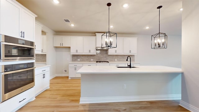 kitchen featuring stainless steel double oven, gas stovetop, sink, pendant lighting, and white cabinets