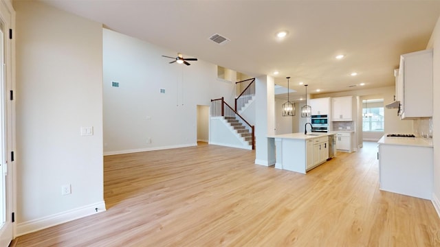 kitchen featuring white cabinets, light hardwood / wood-style flooring, hanging light fixtures, and an island with sink