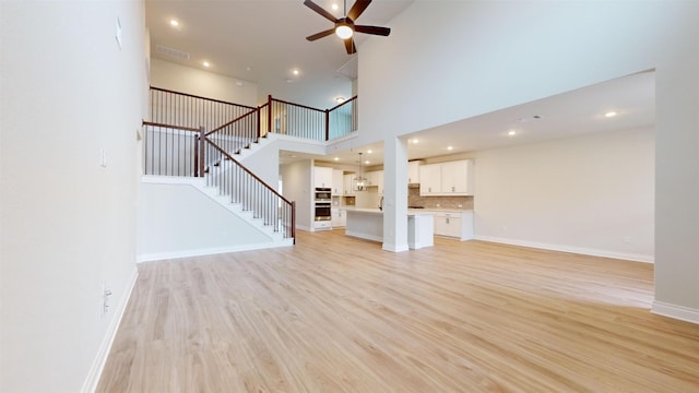 unfurnished living room featuring ceiling fan, sink, light hardwood / wood-style floors, and a high ceiling