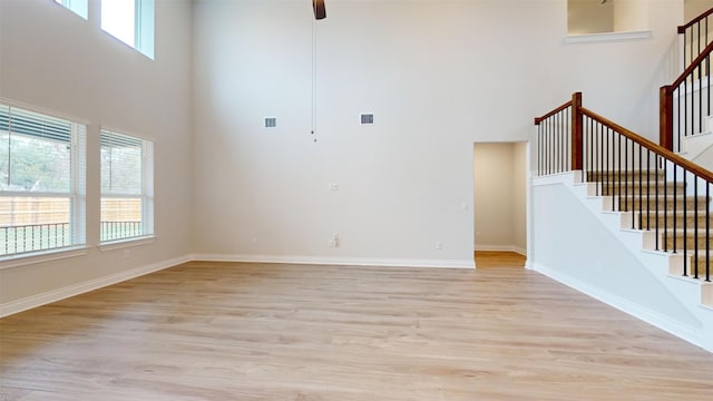 unfurnished living room featuring ceiling fan, light hardwood / wood-style flooring, and a high ceiling