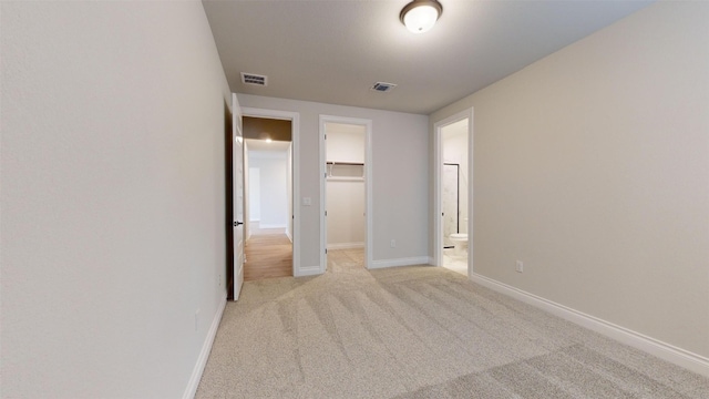 unfurnished bedroom with a walk in closet, light carpet, and a closet