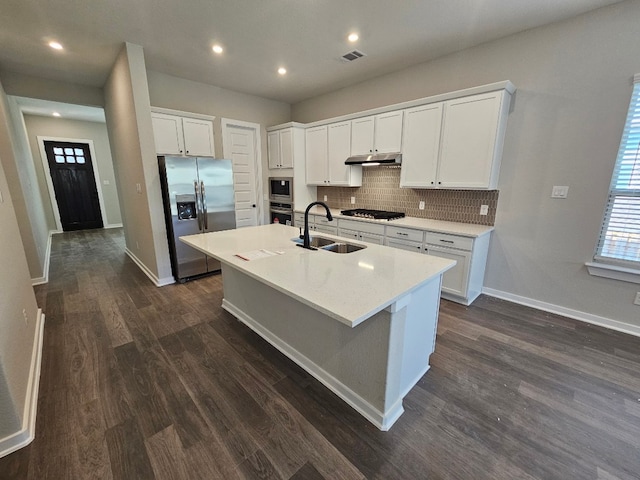1709 Garret Oaks Ln, Georgetown, TX 78633 - kitchen featuring stainless steel appliances, under cabinet range hood, a kitchen island with sink, dark wood-style flooring, and decorative backsplash