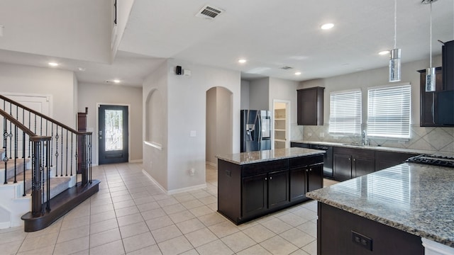 kitchen with light stone counters, a wealth of natural light, a kitchen island, and stainless steel refrigerator with ice dispenser