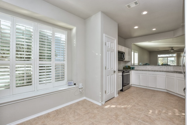 kitchen with decorative backsplash, light tile patterned floors, appliances with stainless steel finishes, white cabinetry, and dark stone counters