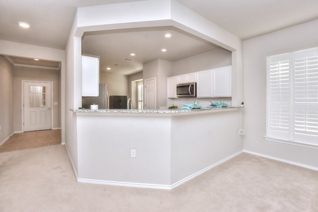 kitchen featuring light carpet, stainless steel appliances, kitchen peninsula, white cabinets, and light stone counters