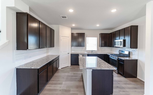 kitchen featuring dark brown cabinets, light wood-type flooring, stainless steel appliances, sink, and a center island