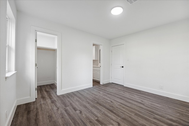 unfurnished bedroom with connected bathroom, a walk in closet, a closet, and dark wood-type flooring