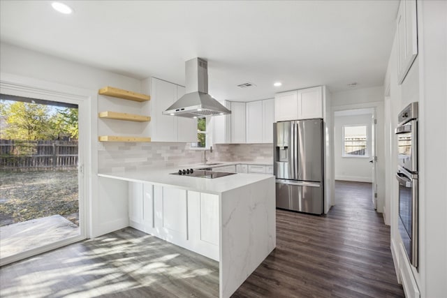 kitchen with island exhaust hood, kitchen peninsula, plenty of natural light, stainless steel fridge, and white cabinetry