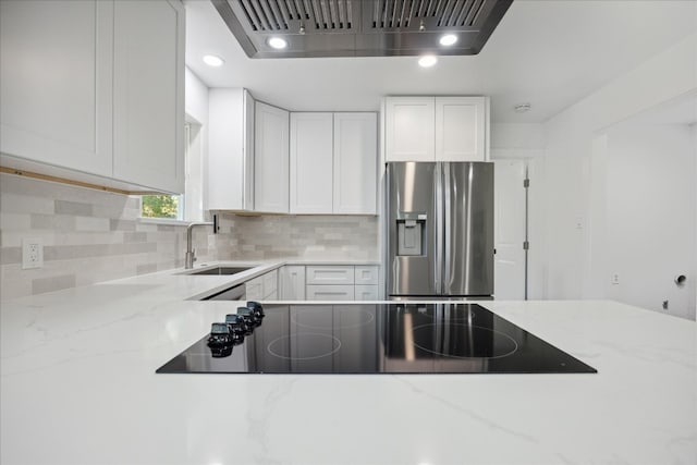 kitchen with stainless steel refrigerator with ice dispenser, white cabinets, light stone counters, and sink