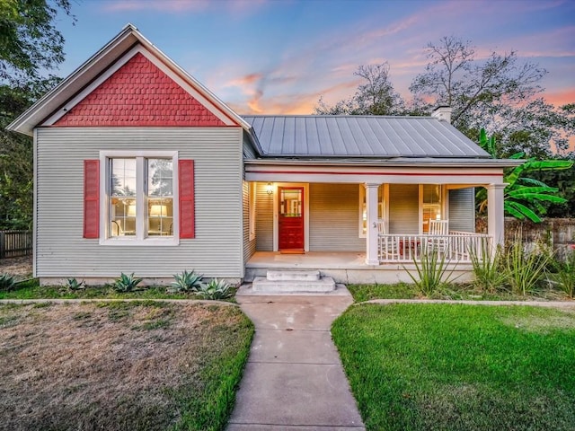 view of front of property featuring a front lawn, covered porch, and metal roof