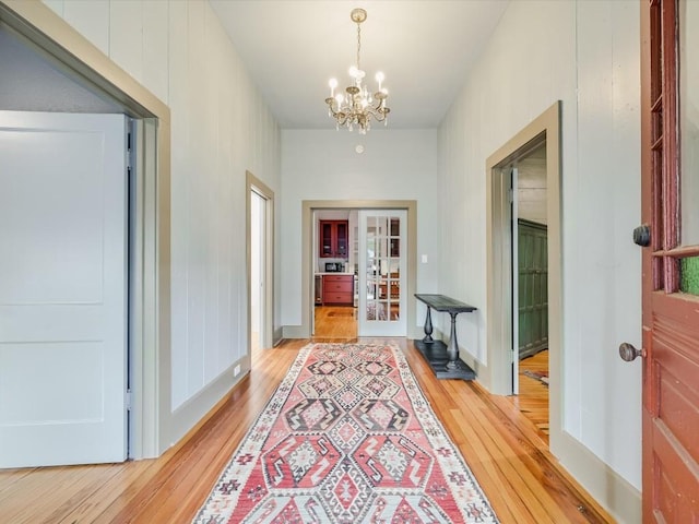 hallway with french doors, light wood-type flooring, and a chandelier