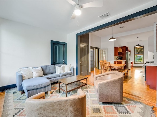 living room with a ceiling fan, visible vents, and light wood-type flooring