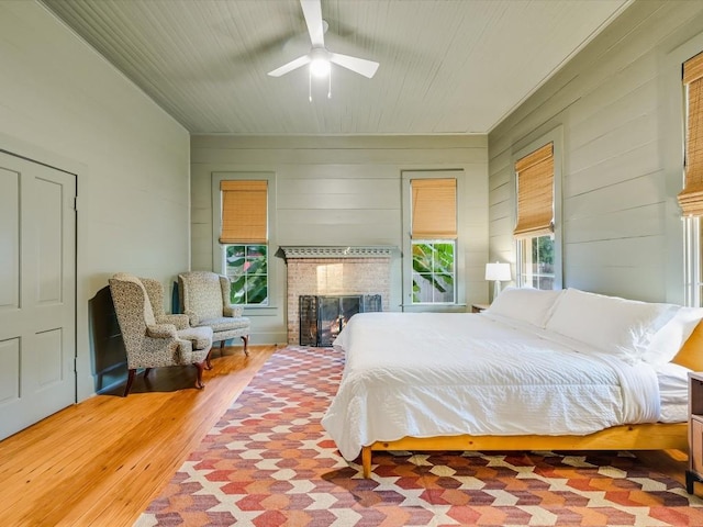 bedroom featuring a ceiling fan, wood walls, a brick fireplace, and wood finished floors