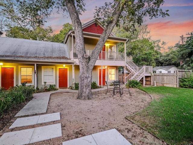 back of house at dusk with stairway, a lawn, fence, and a patio