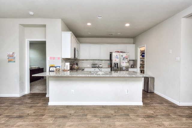 kitchen with appliances with stainless steel finishes, a center island with sink, white cabinetry, and light stone counters