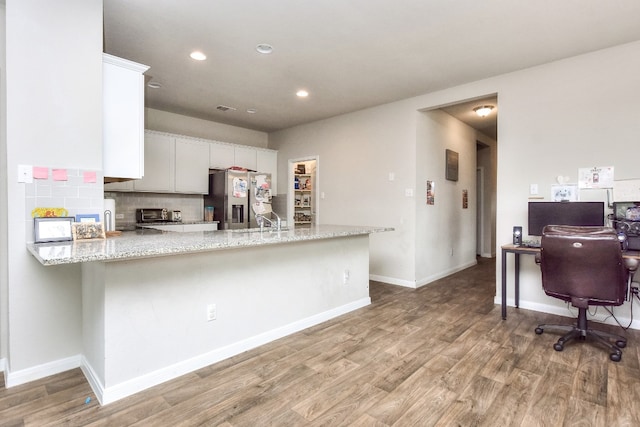 kitchen featuring white cabinets, stainless steel refrigerator with ice dispenser, hardwood / wood-style flooring, light stone countertops, and kitchen peninsula