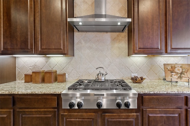 kitchen with wall chimney exhaust hood, light stone countertops, and backsplash