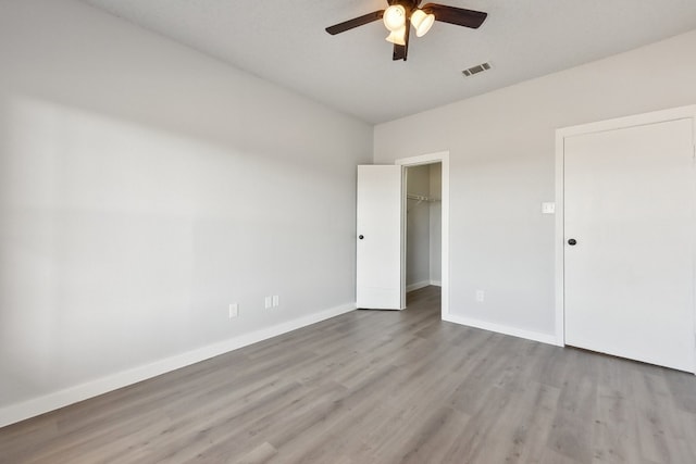 unfurnished bedroom with light hardwood / wood-style flooring, a walk in closet, a closet, and ceiling fan