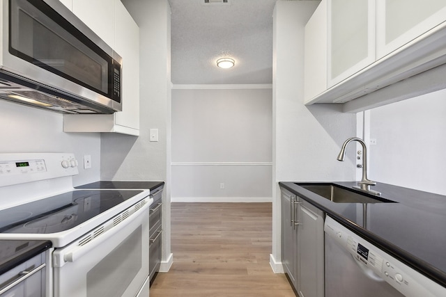 kitchen featuring stainless steel appliances, sink, light wood-type flooring, white cabinetry, and a textured ceiling