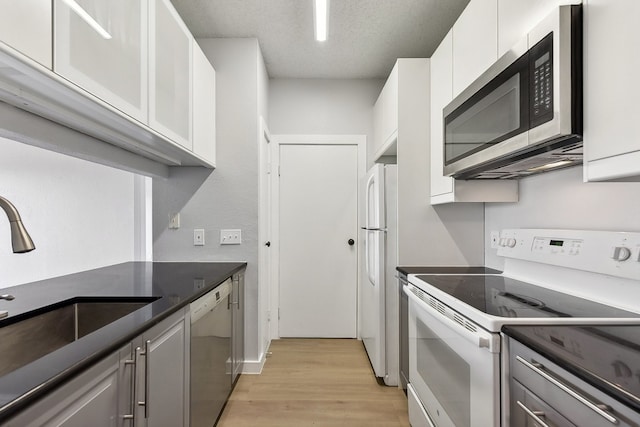 kitchen featuring white appliances, sink, a textured ceiling, white cabinetry, and light hardwood / wood-style floors