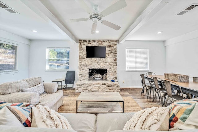 living room featuring beam ceiling, light hardwood / wood-style flooring, a fireplace, and ceiling fan